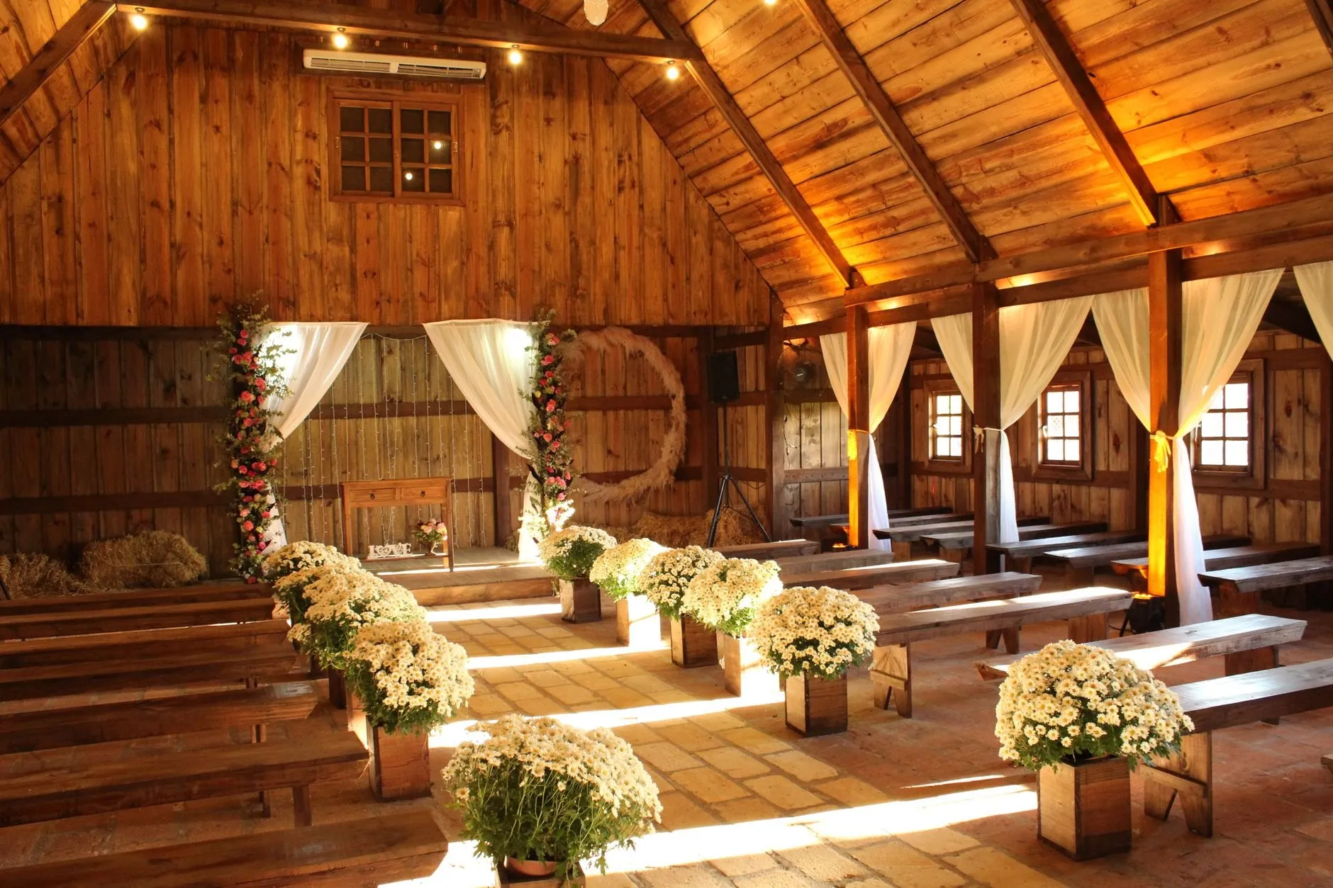 A timber barn set for a ceremony, white flowers in wooden crates along the aisle