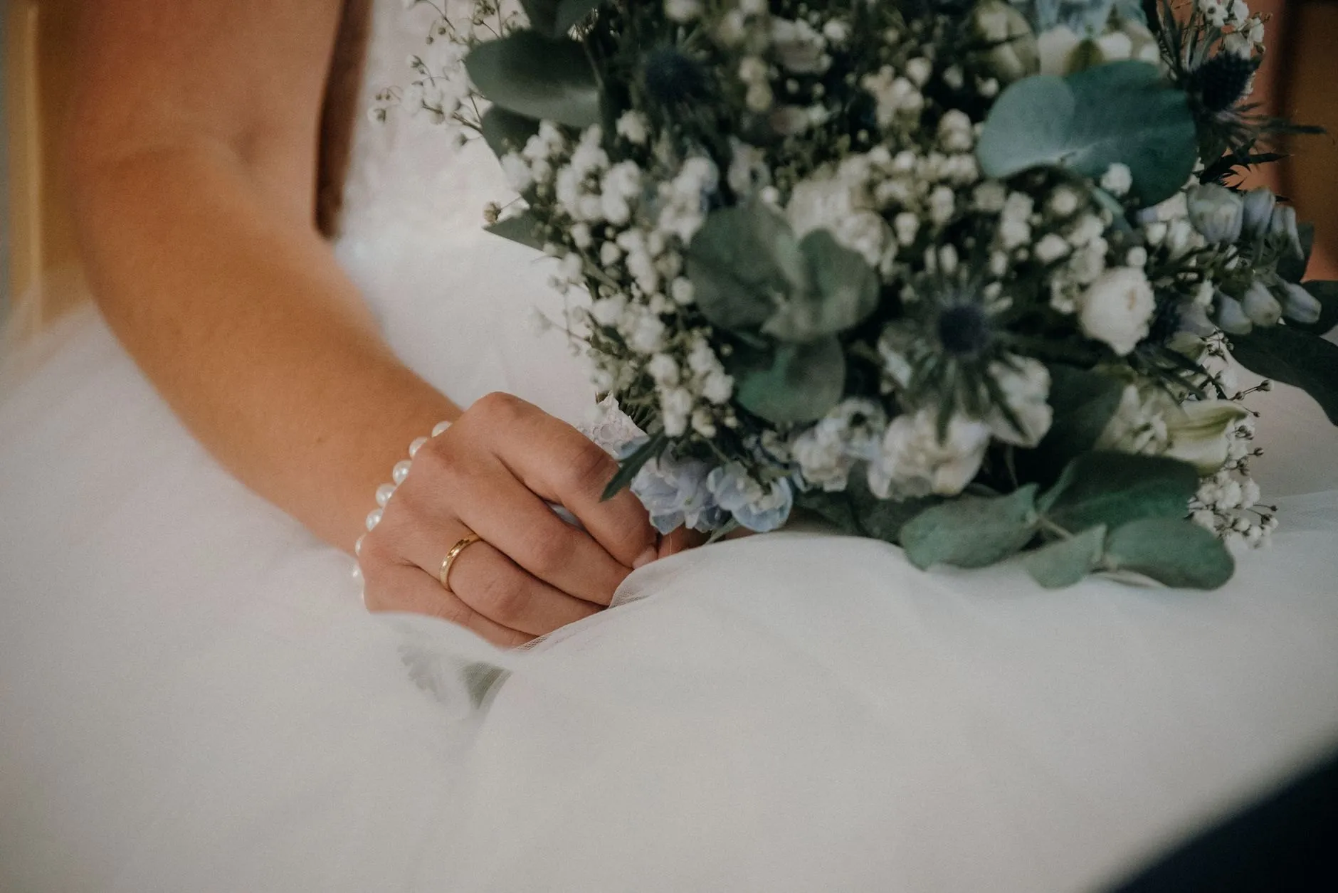 A bride's hand with a pearl bracelet resting on a bouquet of white flowers and eucalyptus