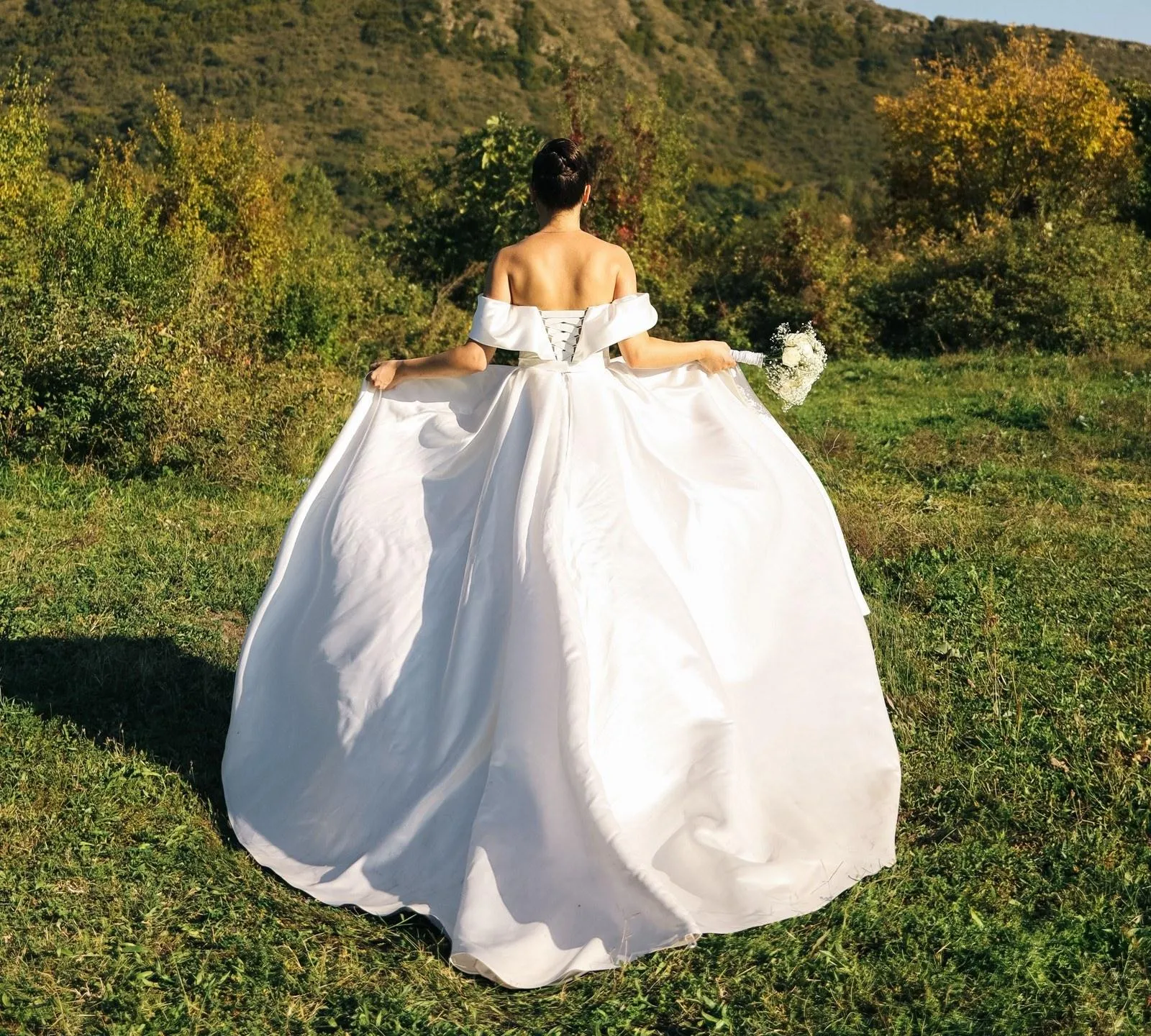 A bride seen from behind walking up a green hillside