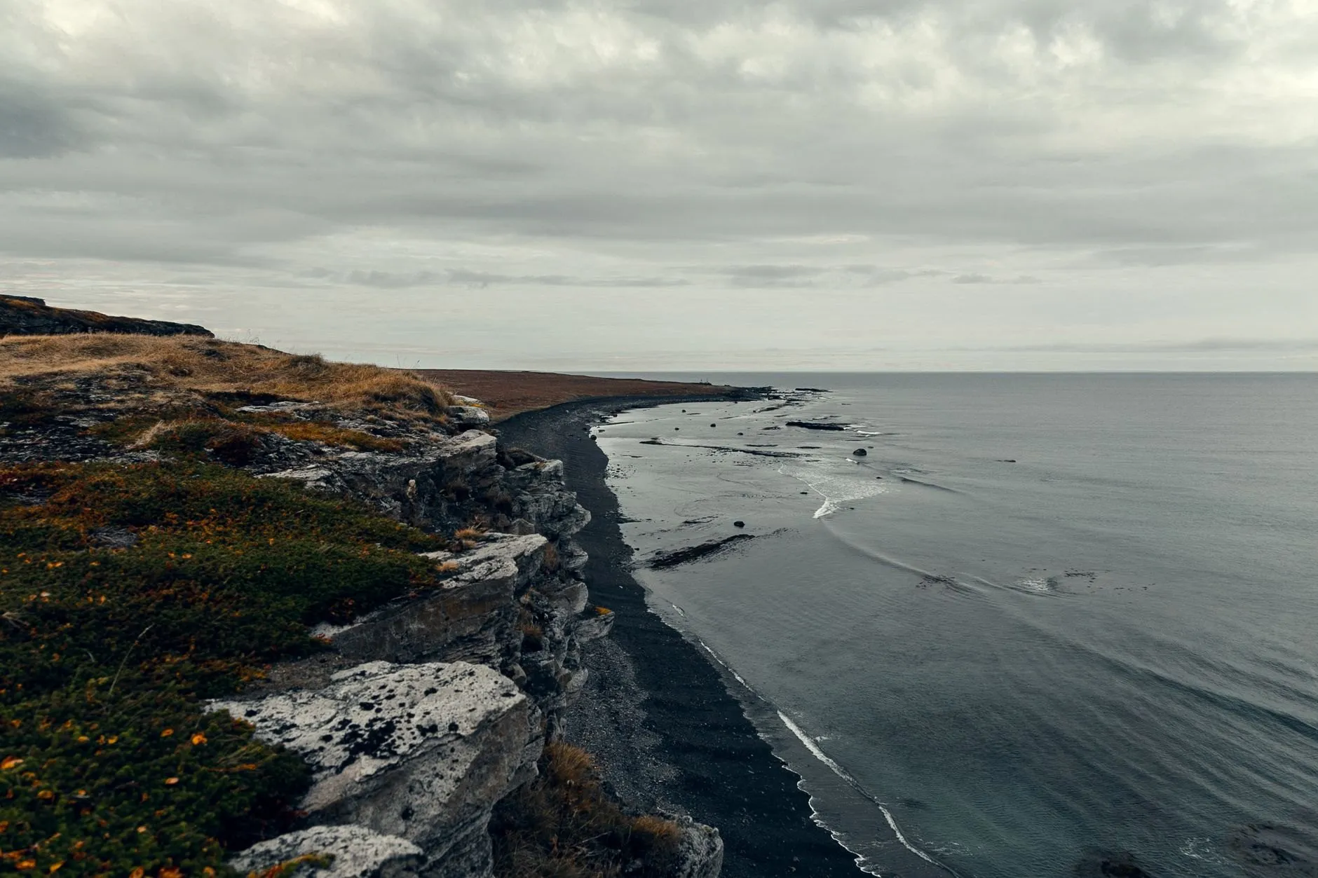 A black sand coastline seen from a cliff top