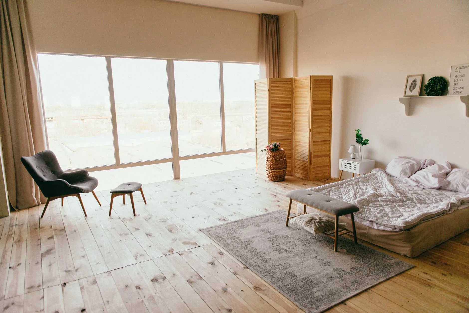 A bright loft bedroom with pale floorboards, a low bed and tall windows