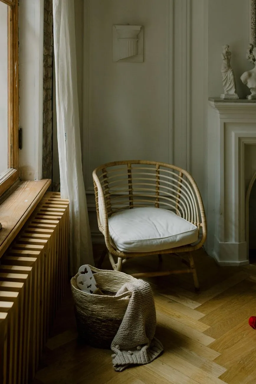 A rattan chair beside a tall window and a white fireplace