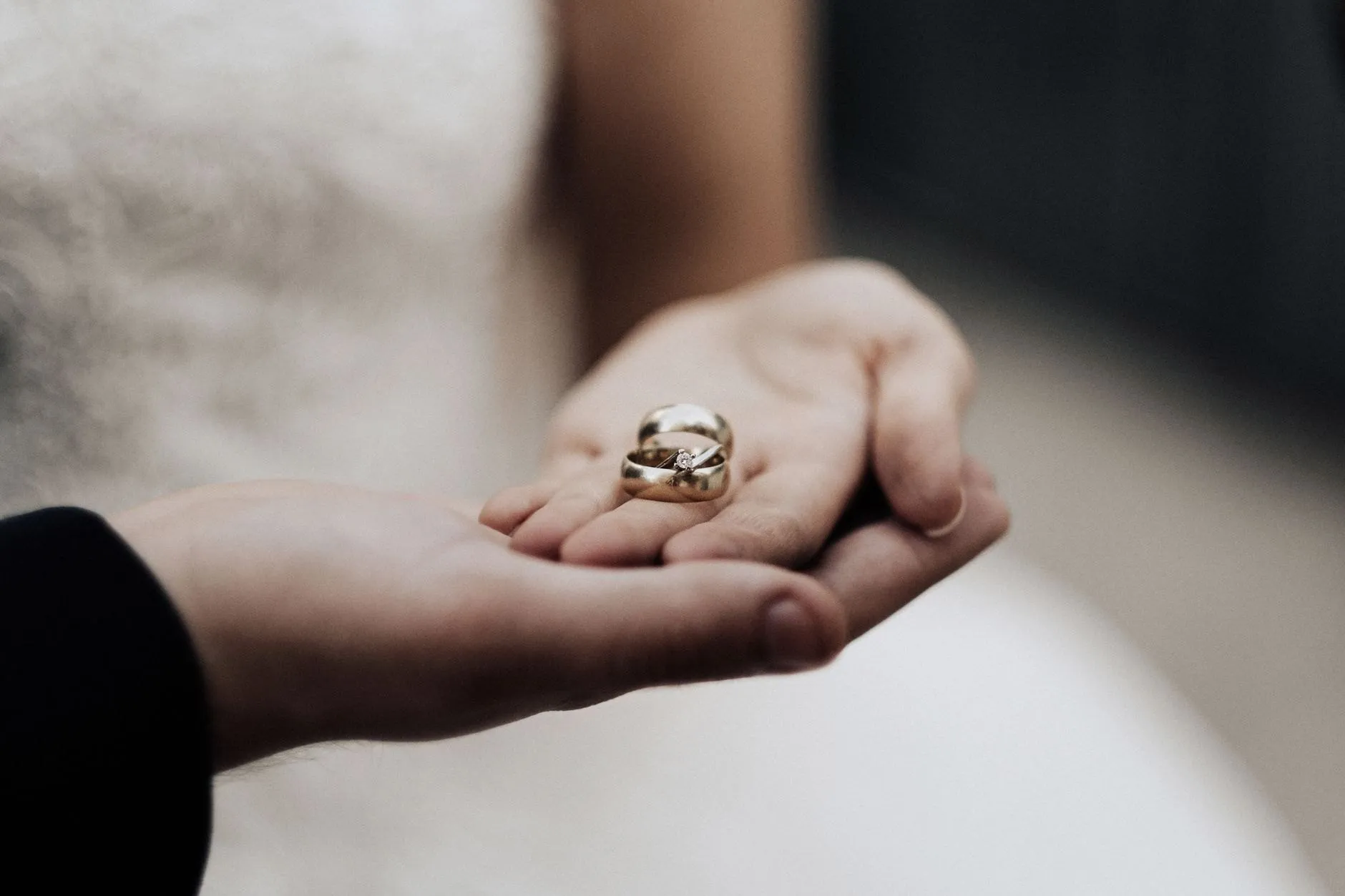 Two wedding rings resting in an open palm against a white dress