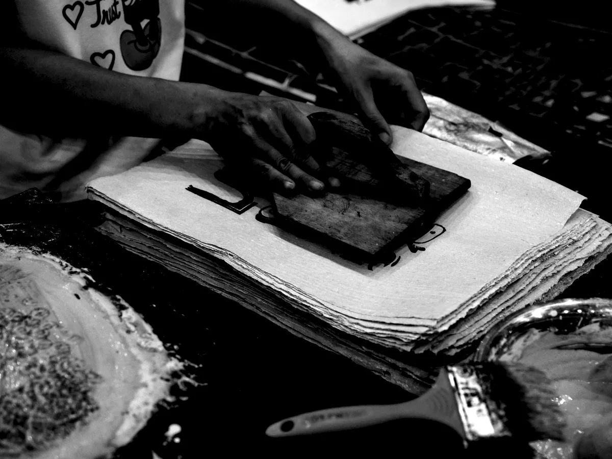 Hands drawing a squeegee across a screen on a stack of sheets.